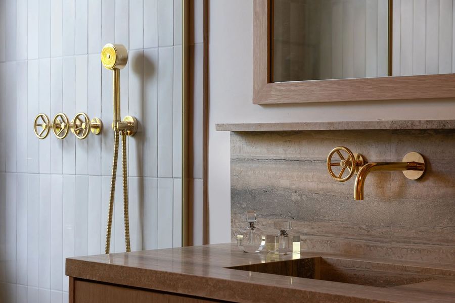 Wall-mounted brass tub filler on stone